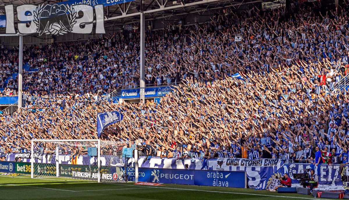 Fondo del Alavés con gran masa albiazul, brazos en alto y la referencia visual de Iraultza 1921